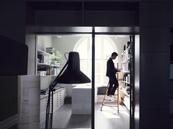 Image of a man standing on a latter by his bookshelf.