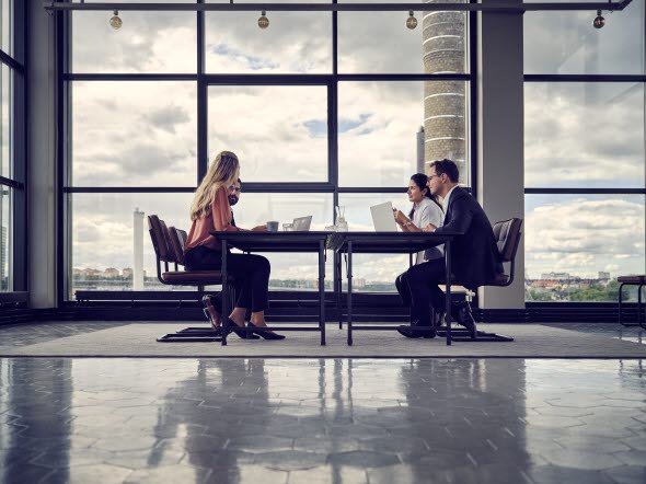 Four people sitting in a meeting room with large windows.