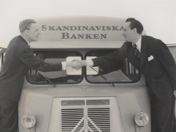 Two men shaking hands while standing on truck labled Skandinaviska Banken