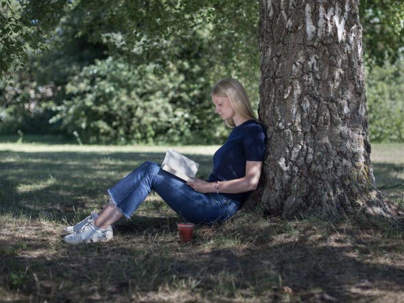 Female student sitting by a tree reading