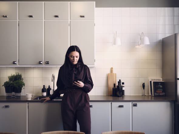 Image of a woman standing in a kitchen and looking at her phone.
