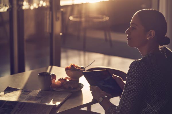 Bild på en kvinna som sitter vid ett matbord med en läsplatta.