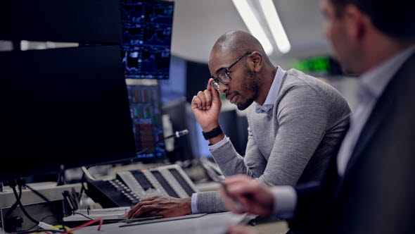 Image of two men sitting in front of computer screens.