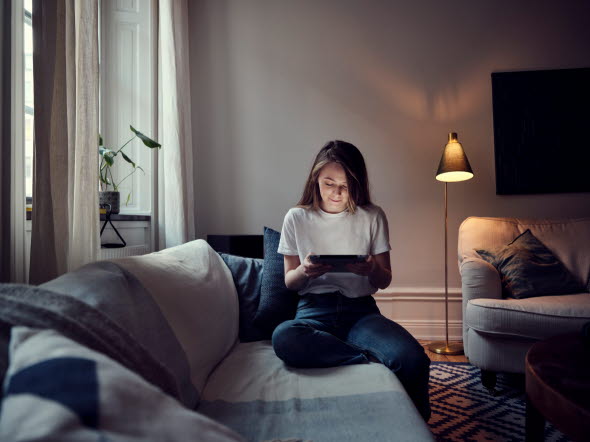Ung kvinna sitter i en soffa och läser på en läsplatta.