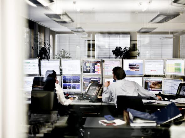 Image of people in front of several computers at an office.