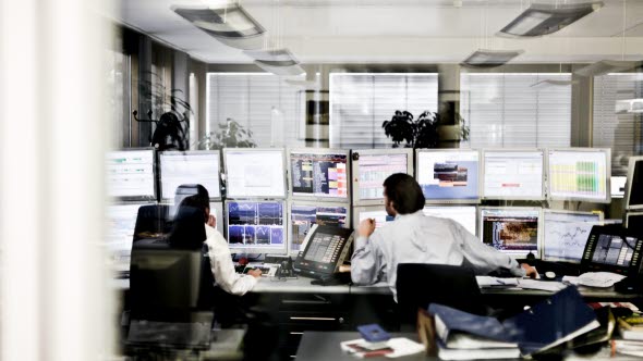 Image of two persons sitting in front of several computer screens.