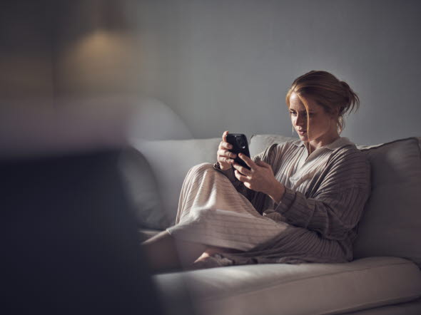 Kvinna tittar på mobilen i soffan
